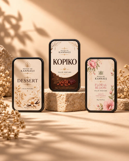 Three rectangular perfume bottles from the brand Kannauj are displayed on stone blocks in a warm, sunlight setting. The bottles feature elegant labels with floral and botanical illustrations, including 'Dessert', 'Kopiko', and 'Floral Bloom' scents.